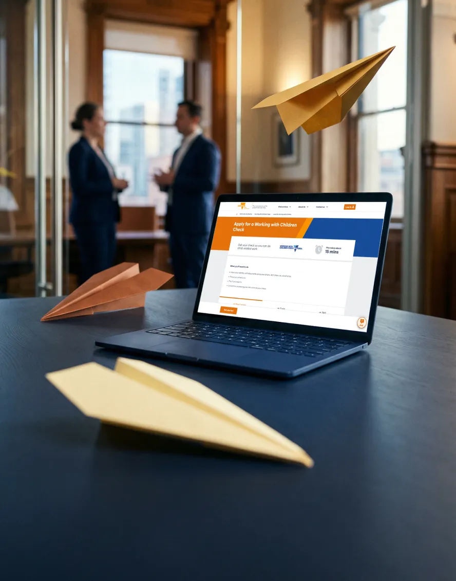 Laptop on a desk shows the Working with Children Check, Victoria website. A man and woman in suits talk in background.