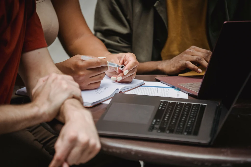 Three people working together with laptops and a notebook at a table.